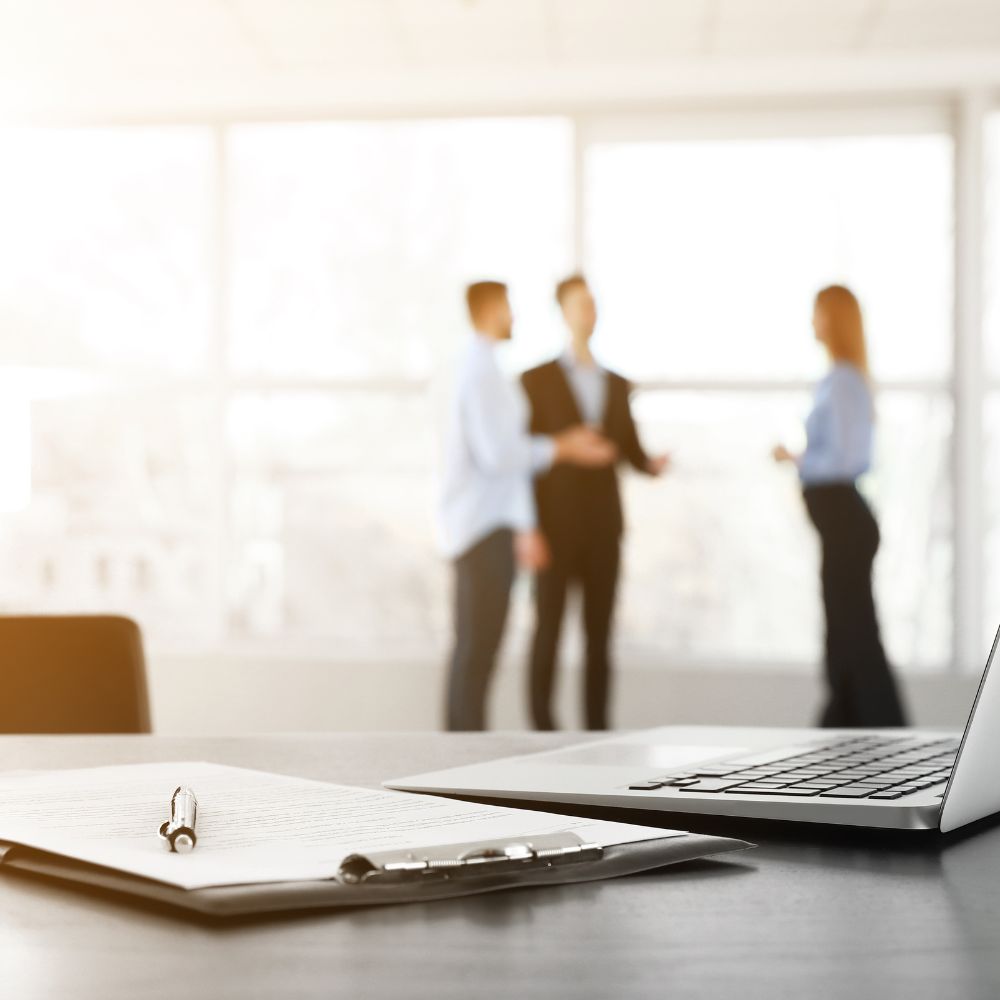 A meeting between business people with a computer and clipboard in the foreground